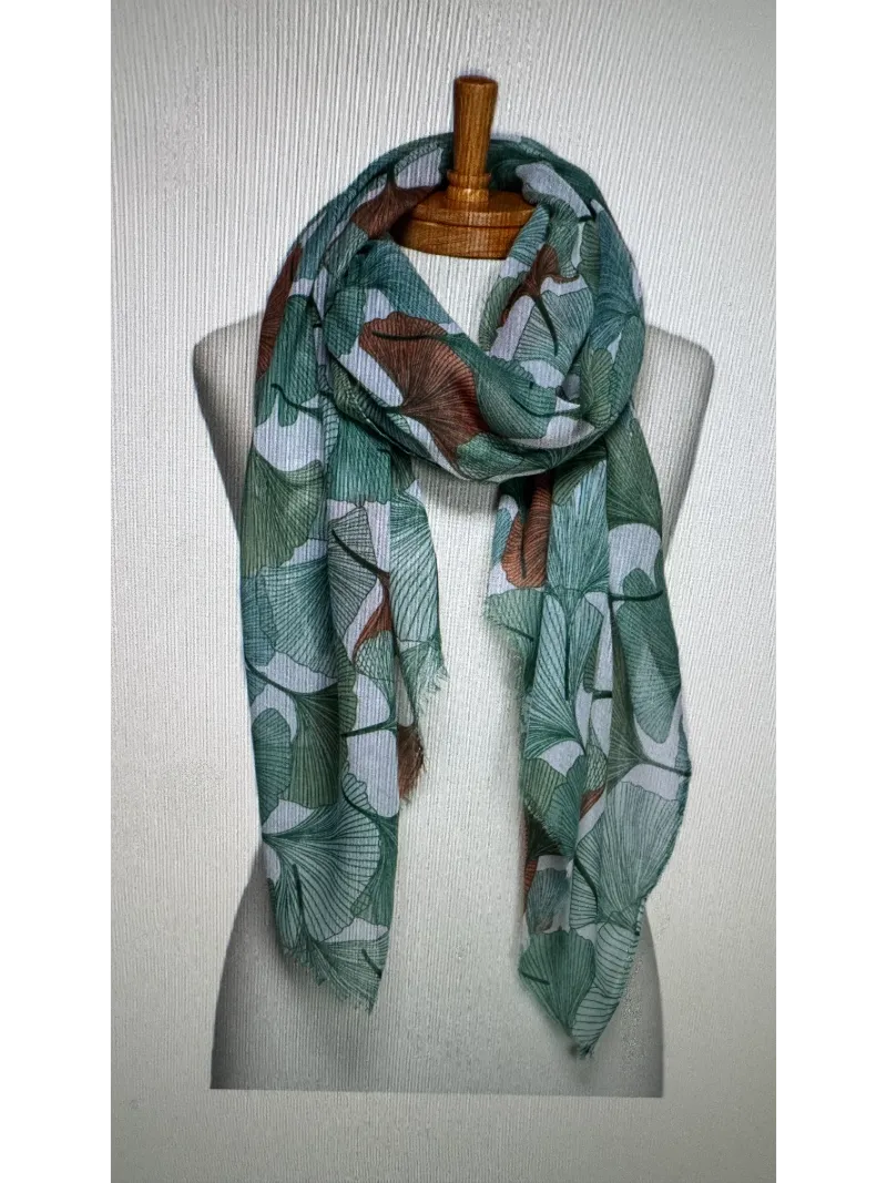A scarf on a mannequin body tied in a front knot with a gingko leaf pattern in different shades of green with hints of terracotta set on a cream background