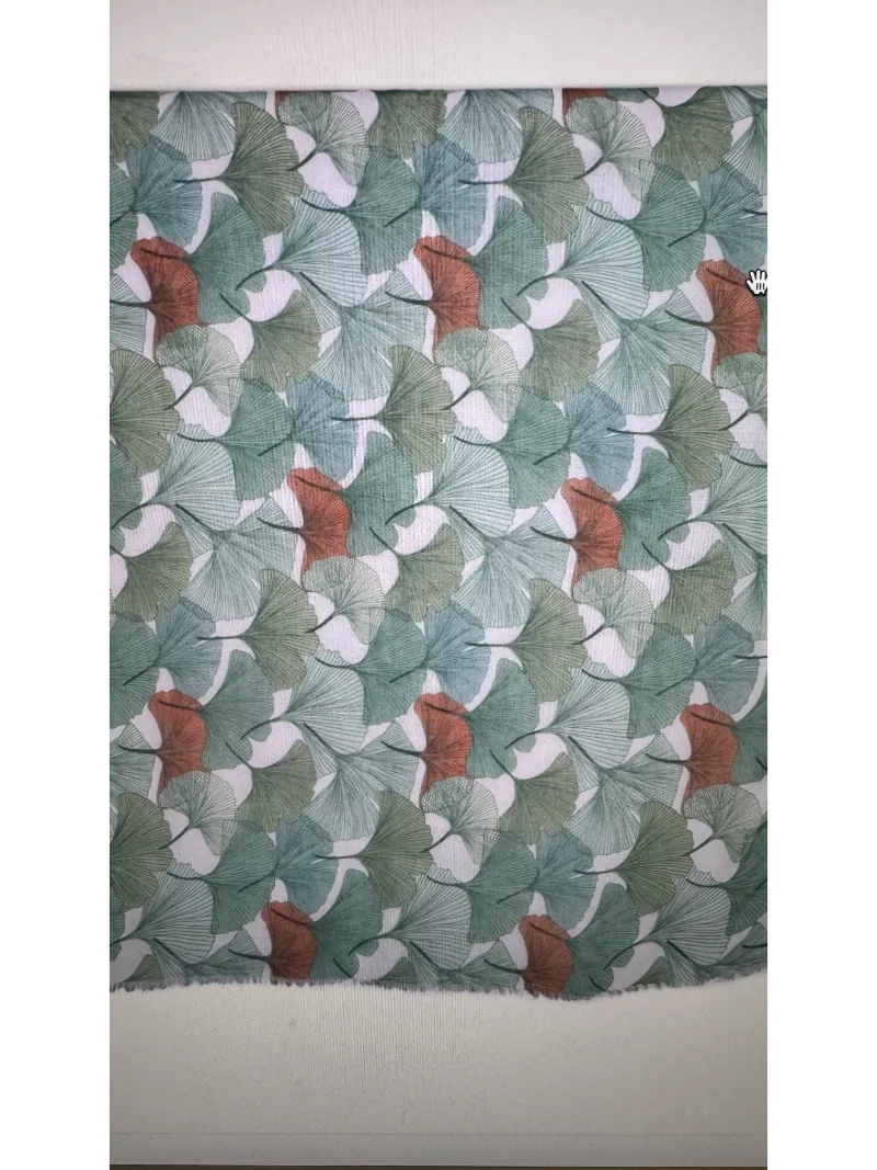 A close up look at a scarf pattern with a gingko leaf design in different shades of green with hints of terracotta set on a cream background