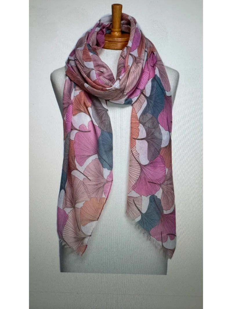 A scarf on a mannequin body tied in a front knot with a gingko leaf pattern in pink,peach and blue colours