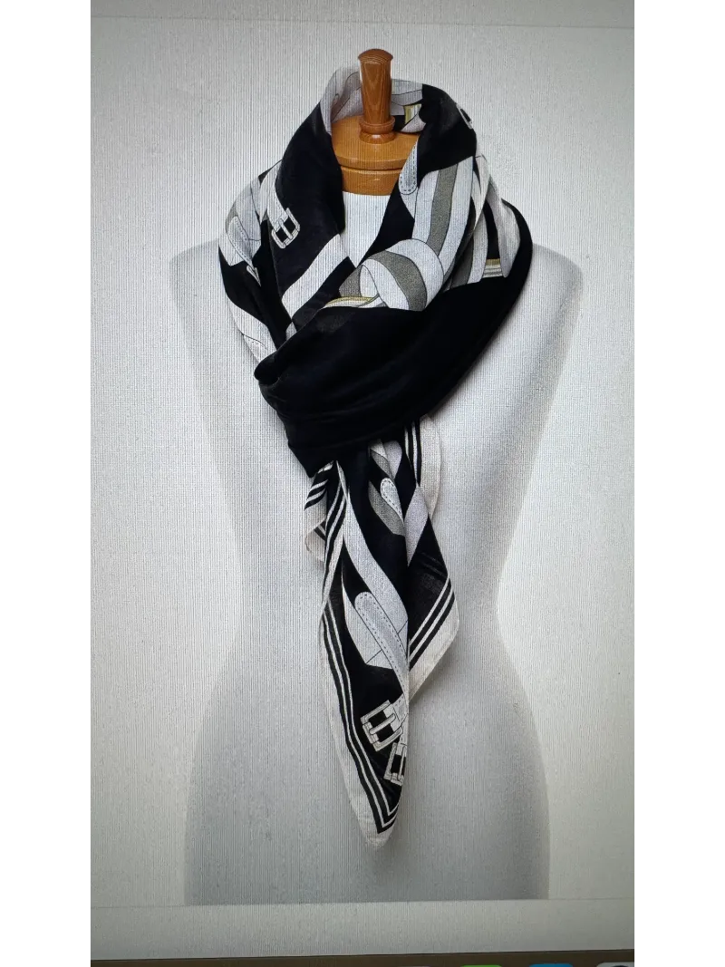 A black , cream and silver scarf on a mannequin body tied in a twist knot with images of belts .