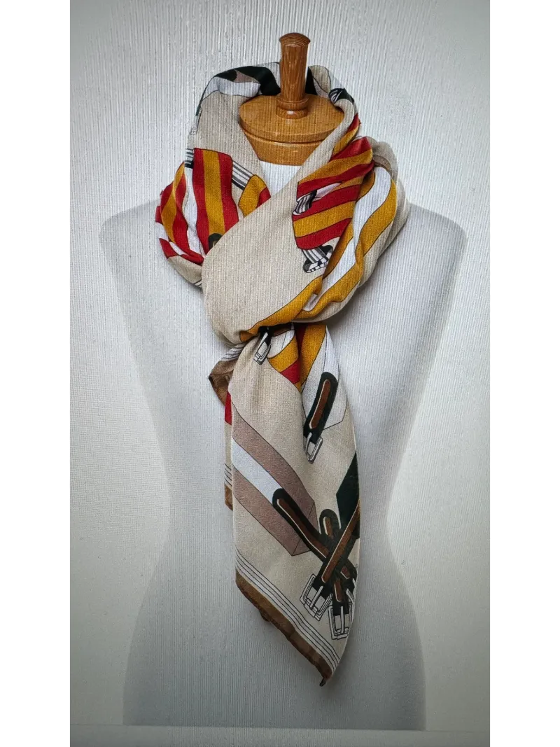 A scarf with a camel base featuring colours of tan red and green on a mannequin body tied in a twist knot ,images of belts